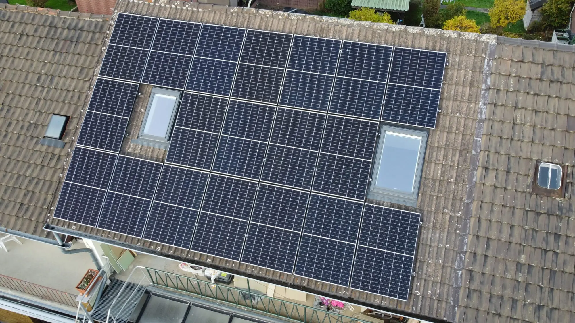 Ziegeldach eines Reihenhauses mit dicht belegten PV-Modulen rund um zwei Dachfenster