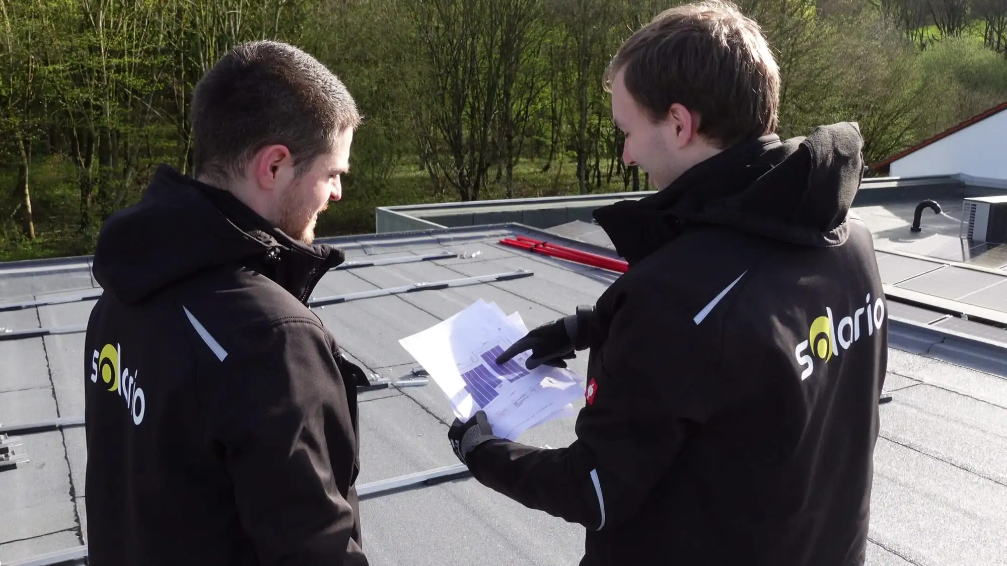 Zwei Solario-Mitarbeiter gehen auf einem Flachdach gemeinsam einen Plan durch