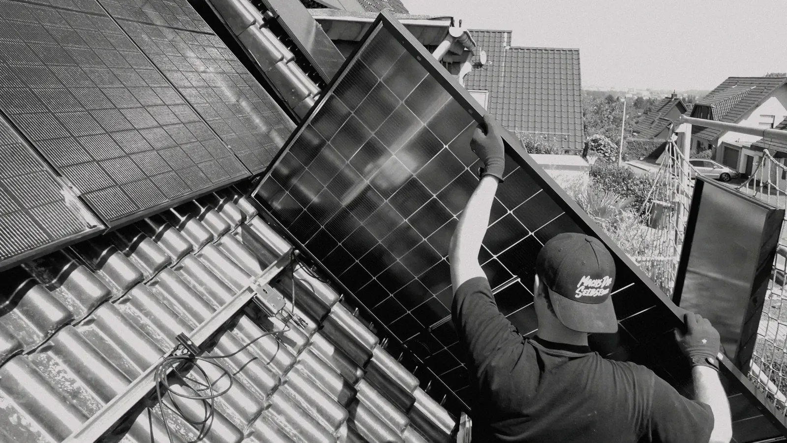 Monteur trägt ein PV-Modul auf ein Ziegeldach