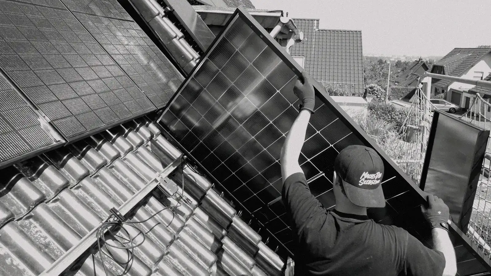 Monteur trägt ein PV-Modul auf ein Ziegeldach